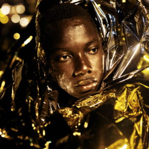 Mediterranean Sea, Italy. Portrait of a migrant man warmed up by a space blanket on the Italian Coast Guard ship "Diciotti".